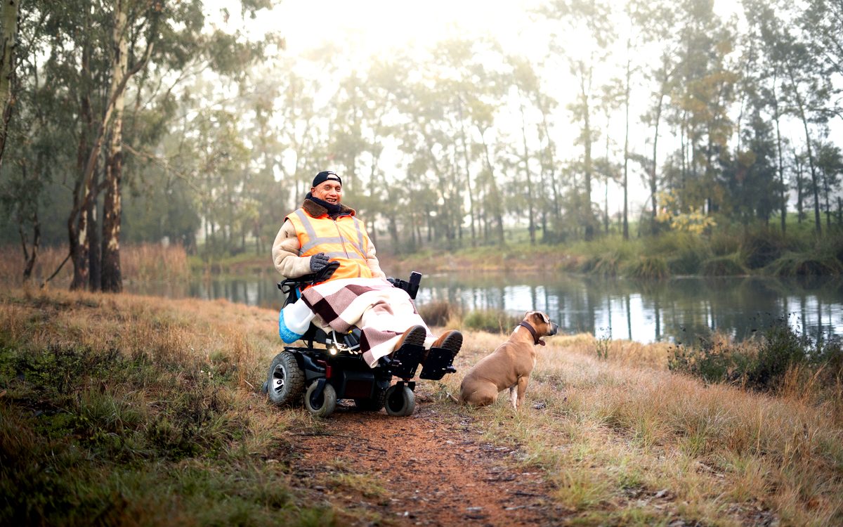 Wilson in his power wheelchair by the river with his dog